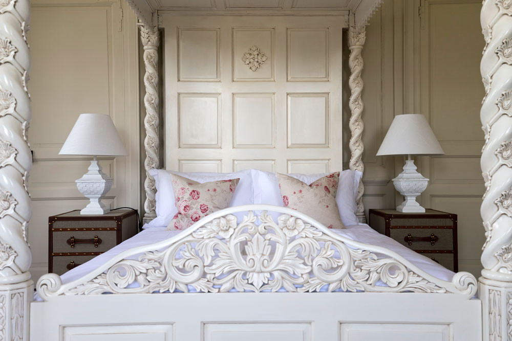Elegant four-poster bed dressed in white bed linen with floral cushions